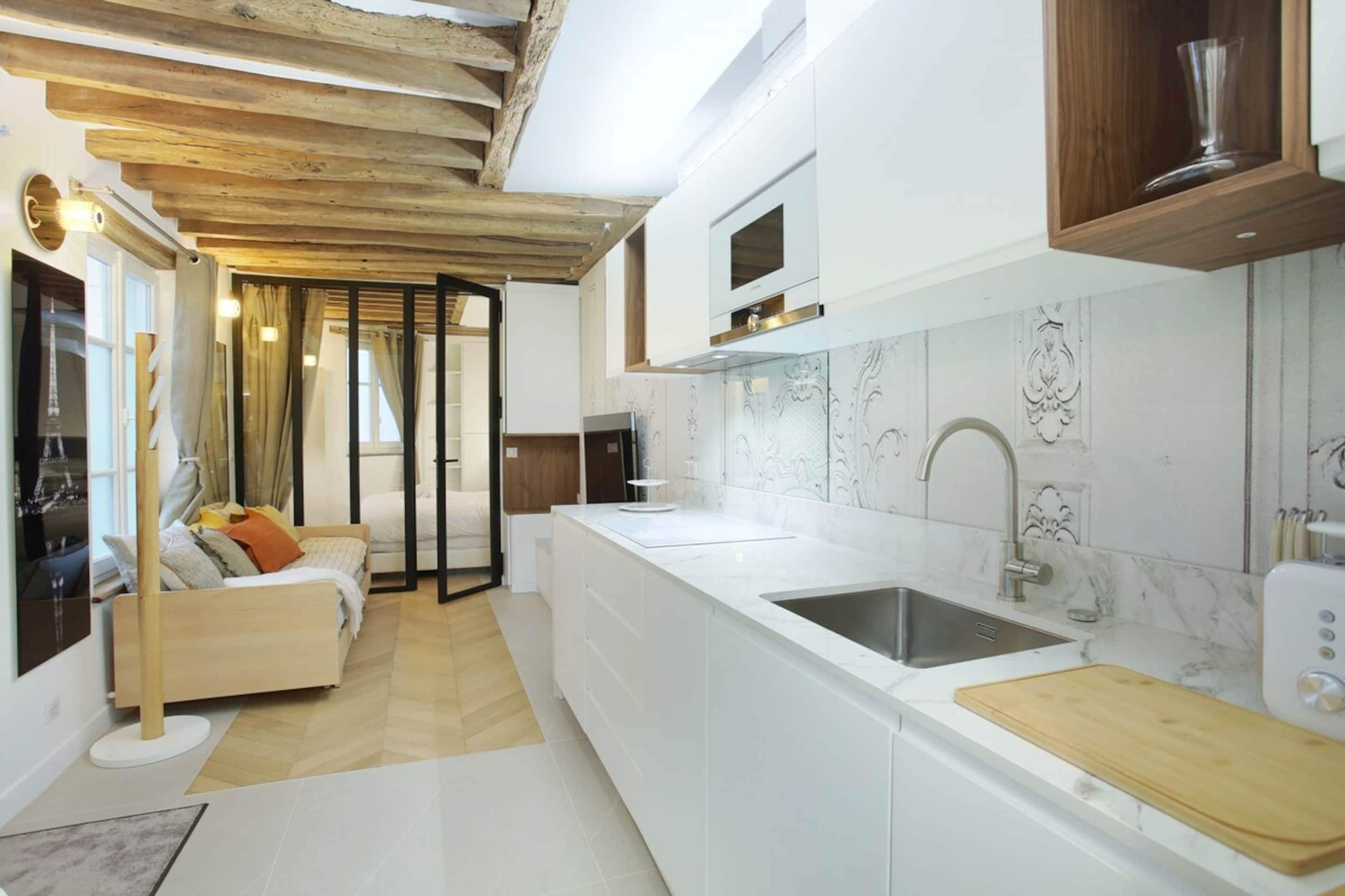 Une cuisine moderne avec des meubles blancs, un pare-feu en marbre et un plafond en bois.