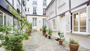 A narrow cobblestone courtyard with potted plants and white-framed windows. - Superb Apartment Place des Vosges Le Marais (Paris)