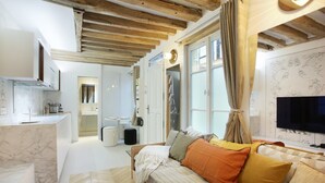 A modern living room with a sofa, a television, and a kitchen area in the background. - Superb Apartment Place des Vosges Le Marais (Paris)