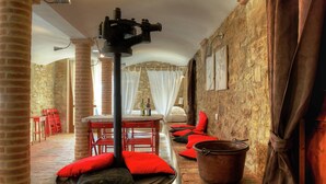 A rustic room with brick walls, a stone floor, red chairs, and a large metal table.