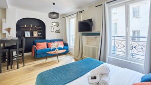 A modern hotel room with a bed, a blue sofa, a dining table, and a TV. - Cosy Apartment Le Marais Center of Paris (Paris)
