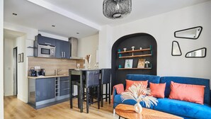 A modern kitchen with grey cabinets and a dining area with a blue sofa and a coffee table. - Cosy Apartment Le Marais Center of Paris (Paris)