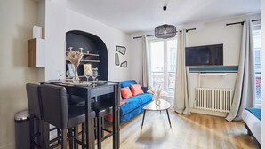A modern living room with a dining area, a blue sofa, and a TV mounted on the wall. - Cosy Apartment Le Marais Center of Paris (Paris)