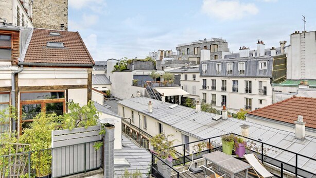 Una terraza en la azotea con vistas a edificios circundantes, incluyendo una torre y una escalera que conduce a un nivel superior.