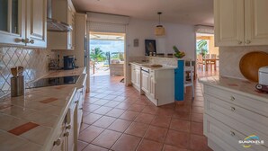 Une cuisine dotée d’un îlot central, de meubles blancs et donnant sur un patio aménagé avec du mobilier d’extérieur.