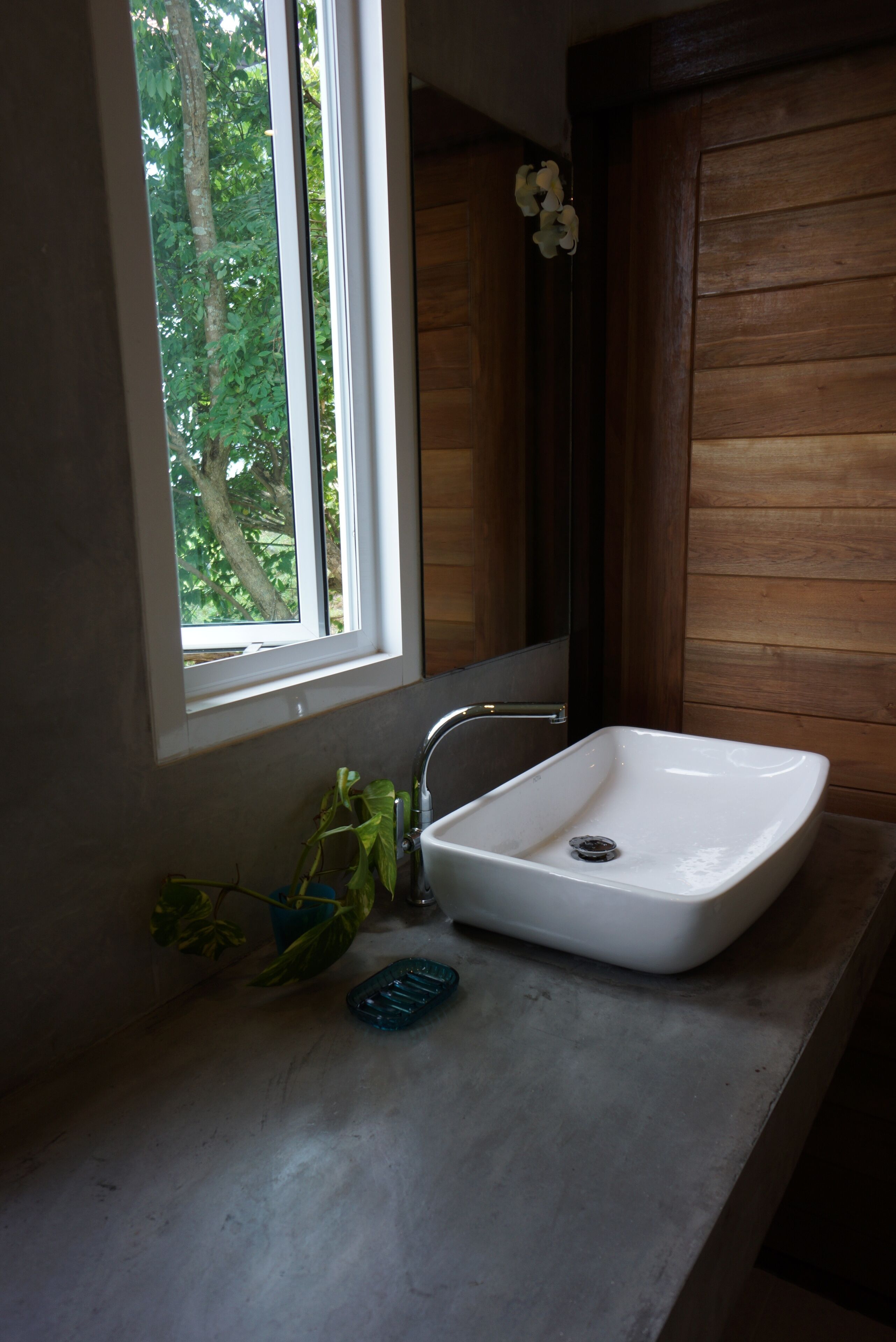 A bathroom with a white sink, a window, and a wooden wall.