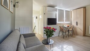 A modern living room with a grey sofa, a small round table with a vase of flowers, and a dining area with a table and chairs.