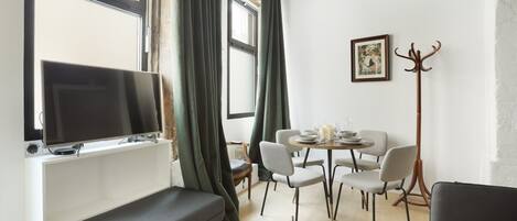 A modern living room with a flat-screen TV, a bench, a dining table with chairs, and a coat rack.