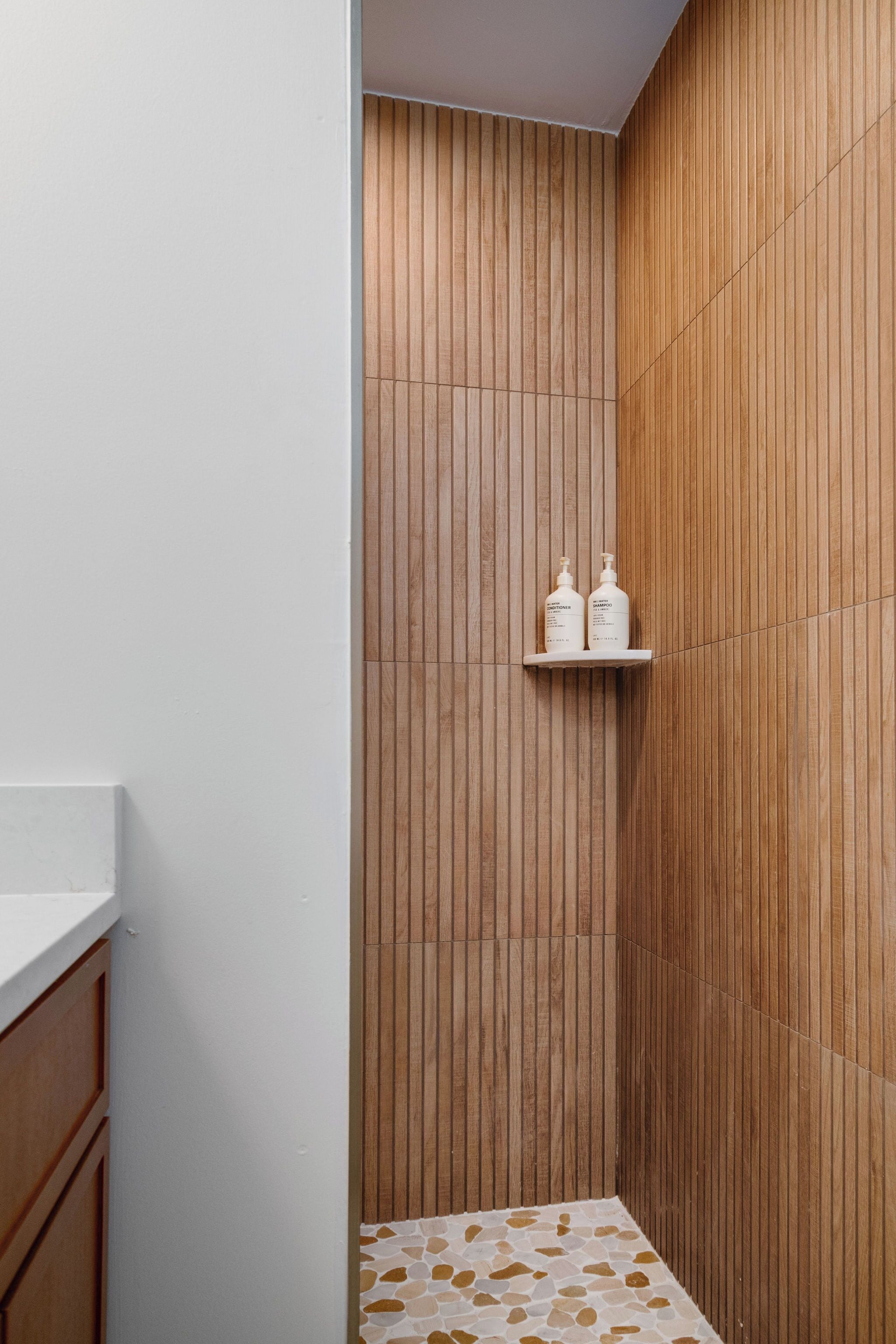 Ein Badezimmer mit Holzverkleidung, einer weißen Ablagefläche und einem Regal mit zwei Flaschen.