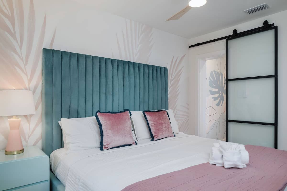 Una cama bien hecha con un cabecero verde azulado, ropa de cama blanca y almohadas rosadas.