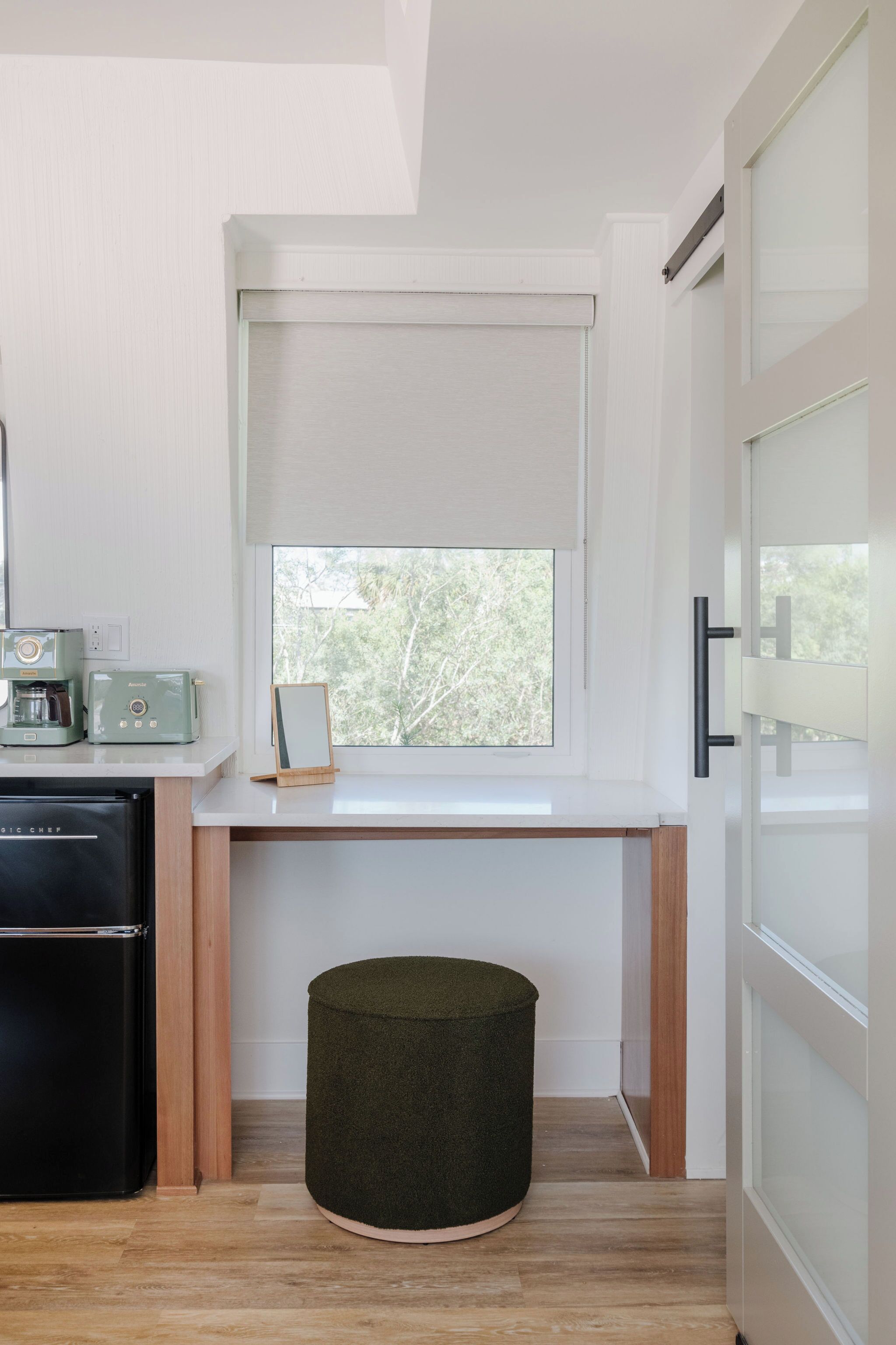 A compact kitchen with a built-in refrigerator, a coffee maker, and a window with a view of trees.