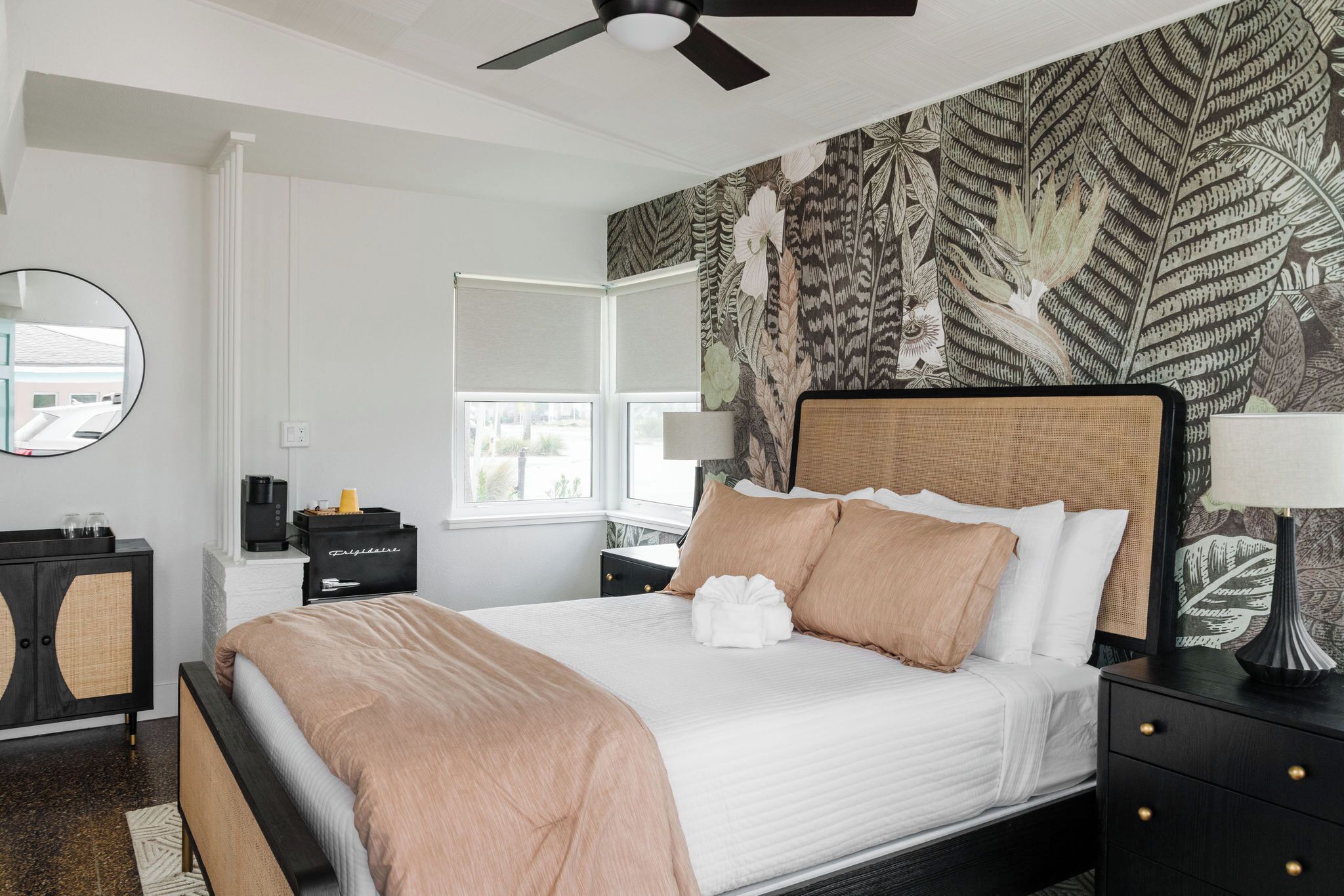 A neatly arranged bedroom with a bed, bedside tables, a ceiling fan, and a window with a view.