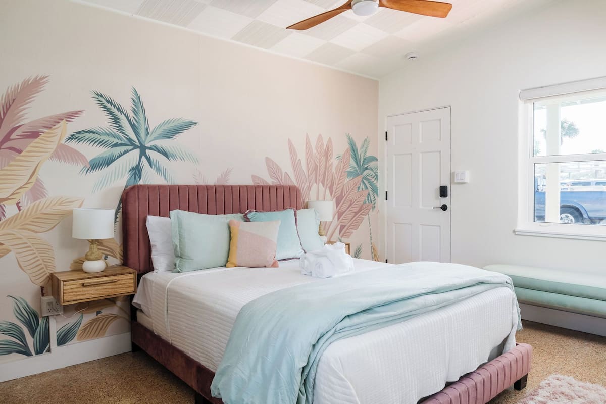 Un dormitorio con cama, mesita de noche, ventana y puerta.