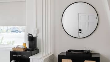 Een moderne hotelkamer met een open haard, een koffieapparaat, een zwarte console tafel met glazen en een ronde spiegel aan de muur.