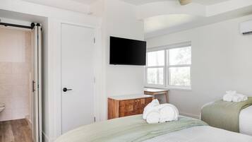 Quarto com cama, penteadeira de madeira, televisão na parede e janela.
