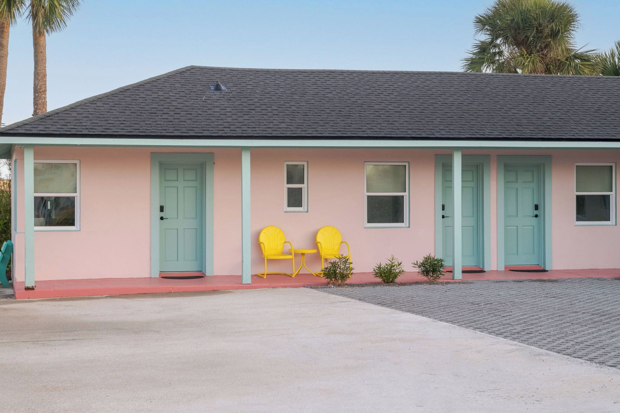 A pink building with teal doors and windows, two yellow chairs outside, and a paved driveway.