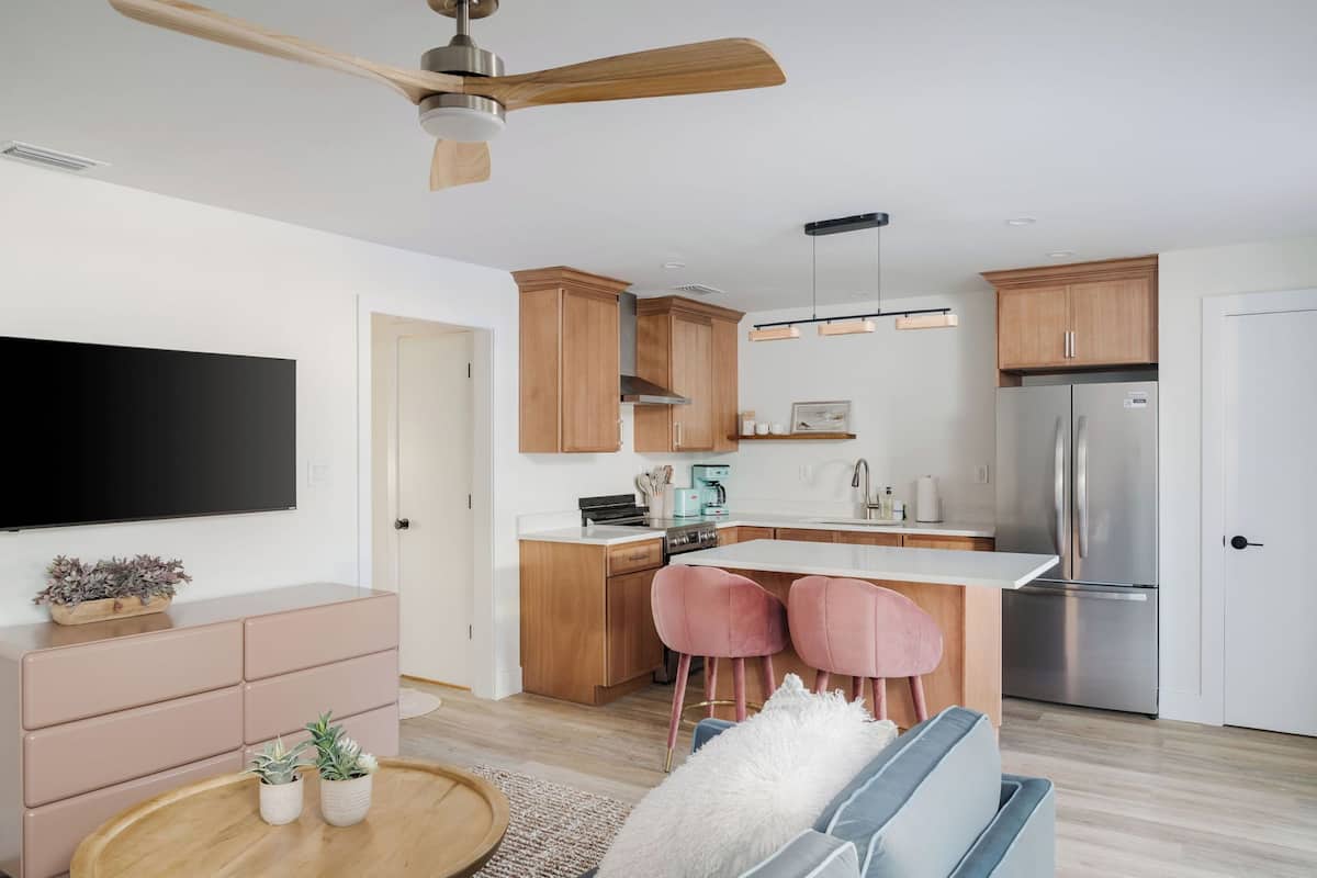 Una cocina moderna con armarios de madera, un refrigerador de acero inoxidable, un televisor de pantalla plana y un comedor con sillas rosas.