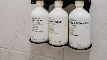 A bathroom with three bottles of shampoo, conditioner, and hand & body wash on a wall-mounted dispenser.