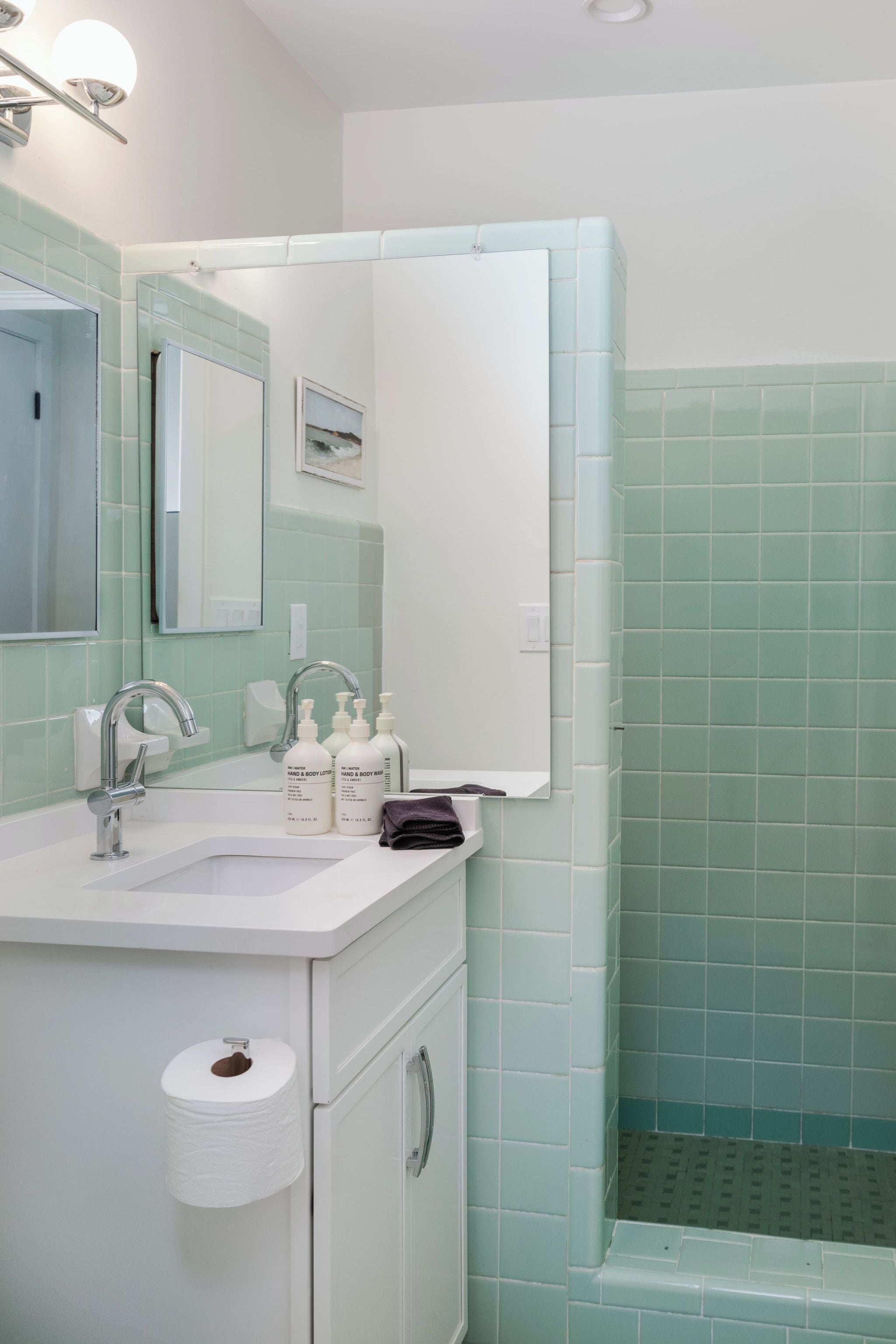 A bathroom with a white sink, mirror, and green-tiled shower.