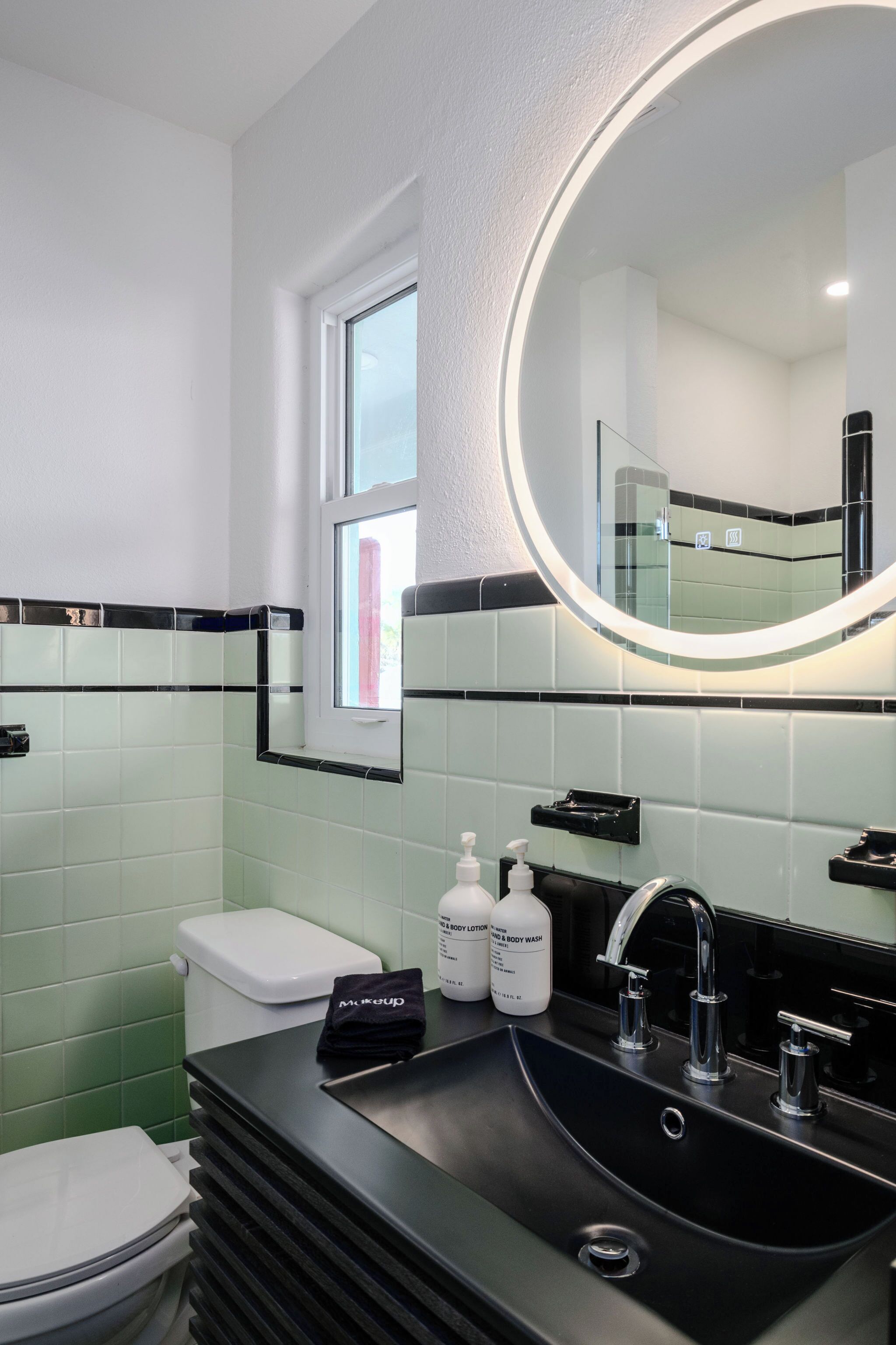 A modern bathroom with a black sink, a round mirror, and a toilet.