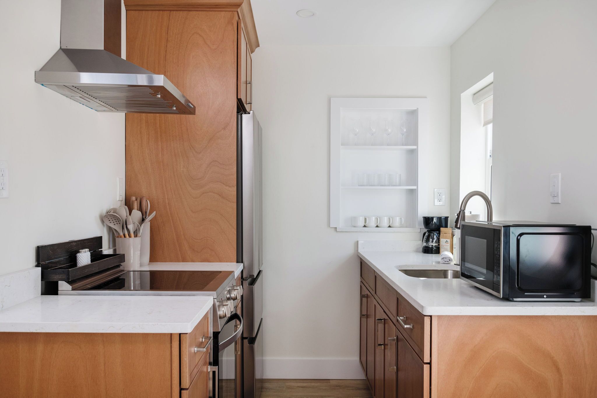 A modern kitchen with a stainless steel range hood, wooden cabinets, a built-in oven, and a microwave on the countertop.