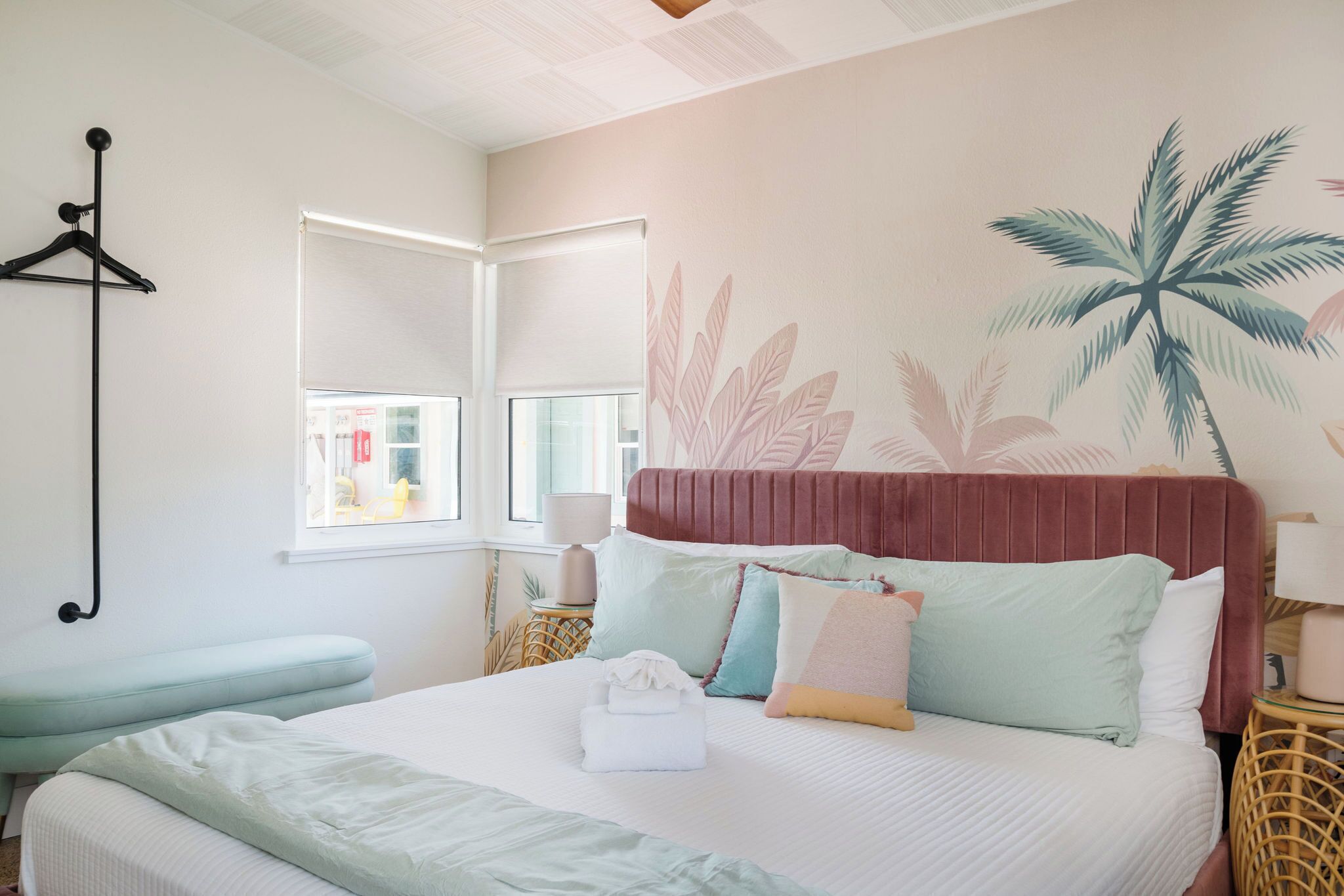Una camera da letto ordinata con un letto, cuscini, un comodino, una rastrelliera per cappotti e una finestra con vista.