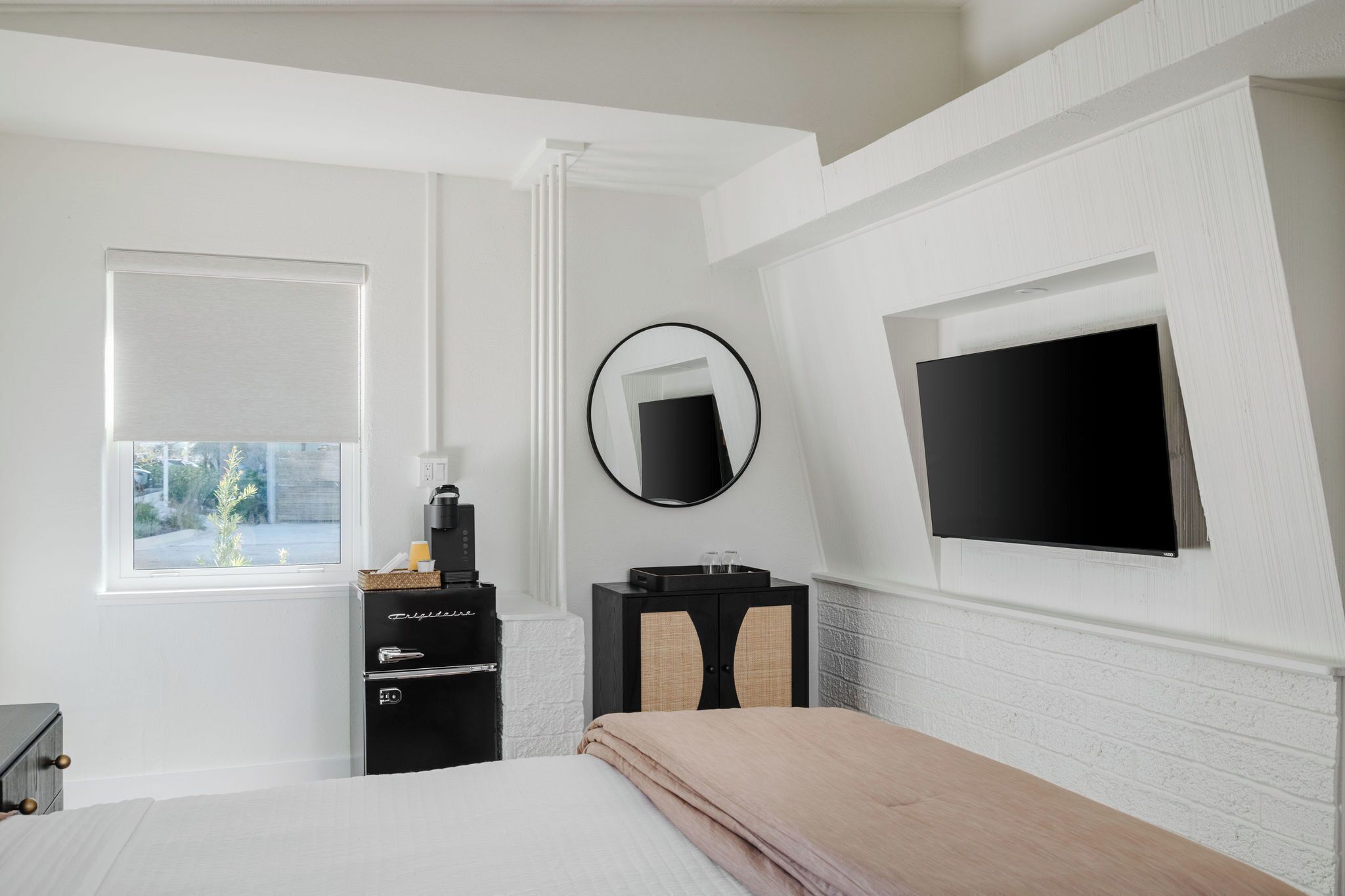 Une chambre à coucher comprenant un lit, une commode, un miroir, un téléviseur et une fenêtre avec des stores.