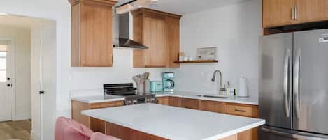 A modern kitchen with wooden cabinets, a stainless steel refrigerator, a coffee maker, and a pink chair.