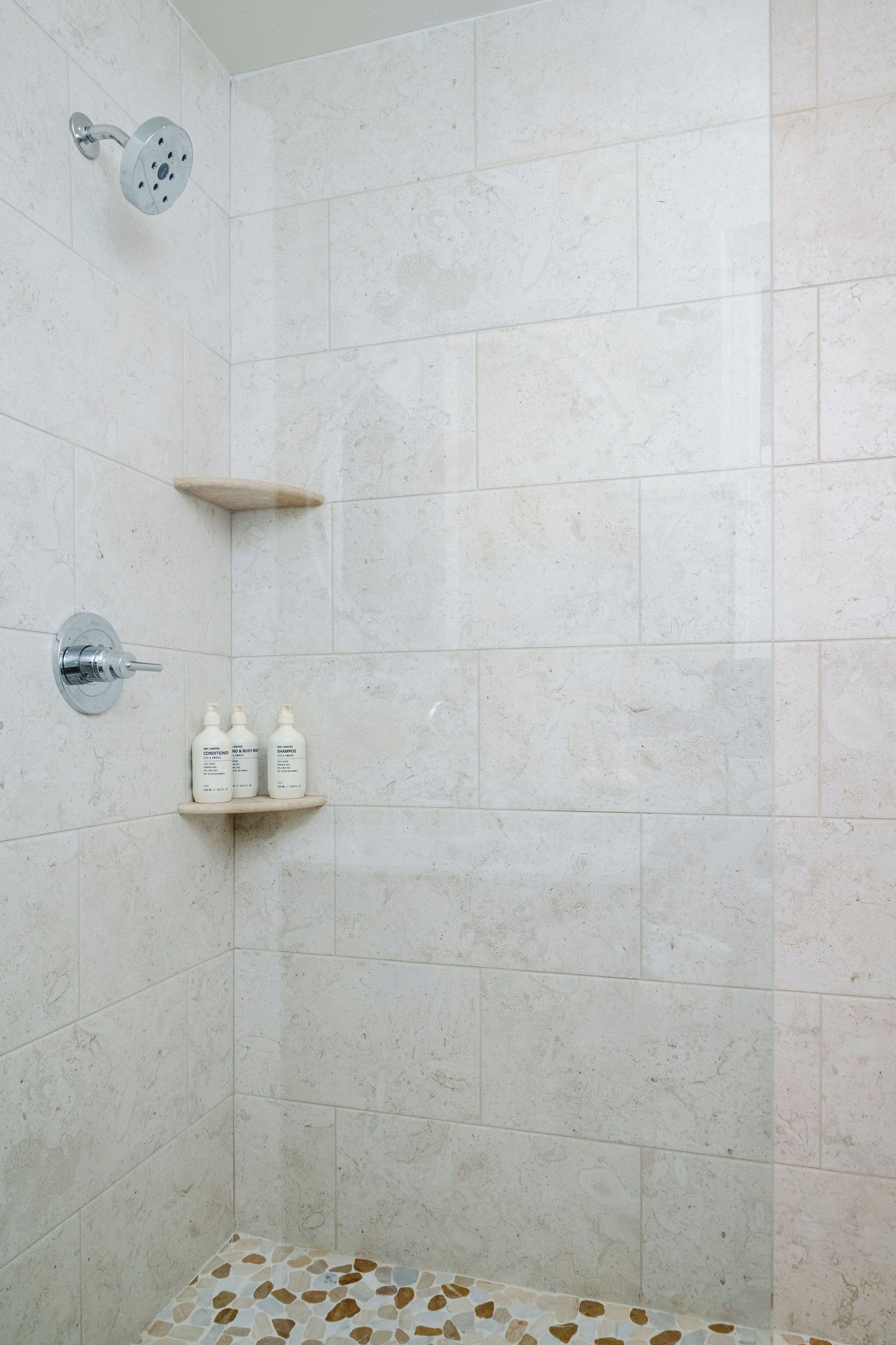 A shower area with a handheld showerhead, a wall-mounted faucet, and a shelf with three bottles.