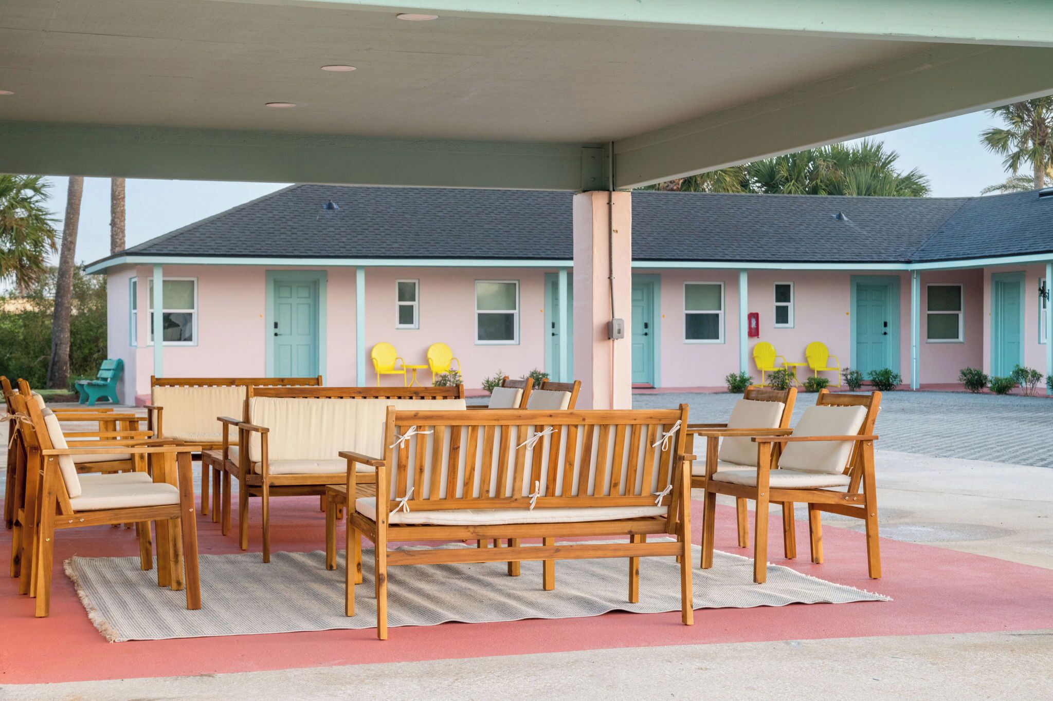 A motel with a covered outdoor seating area, multiple rooms, and a small pool.
