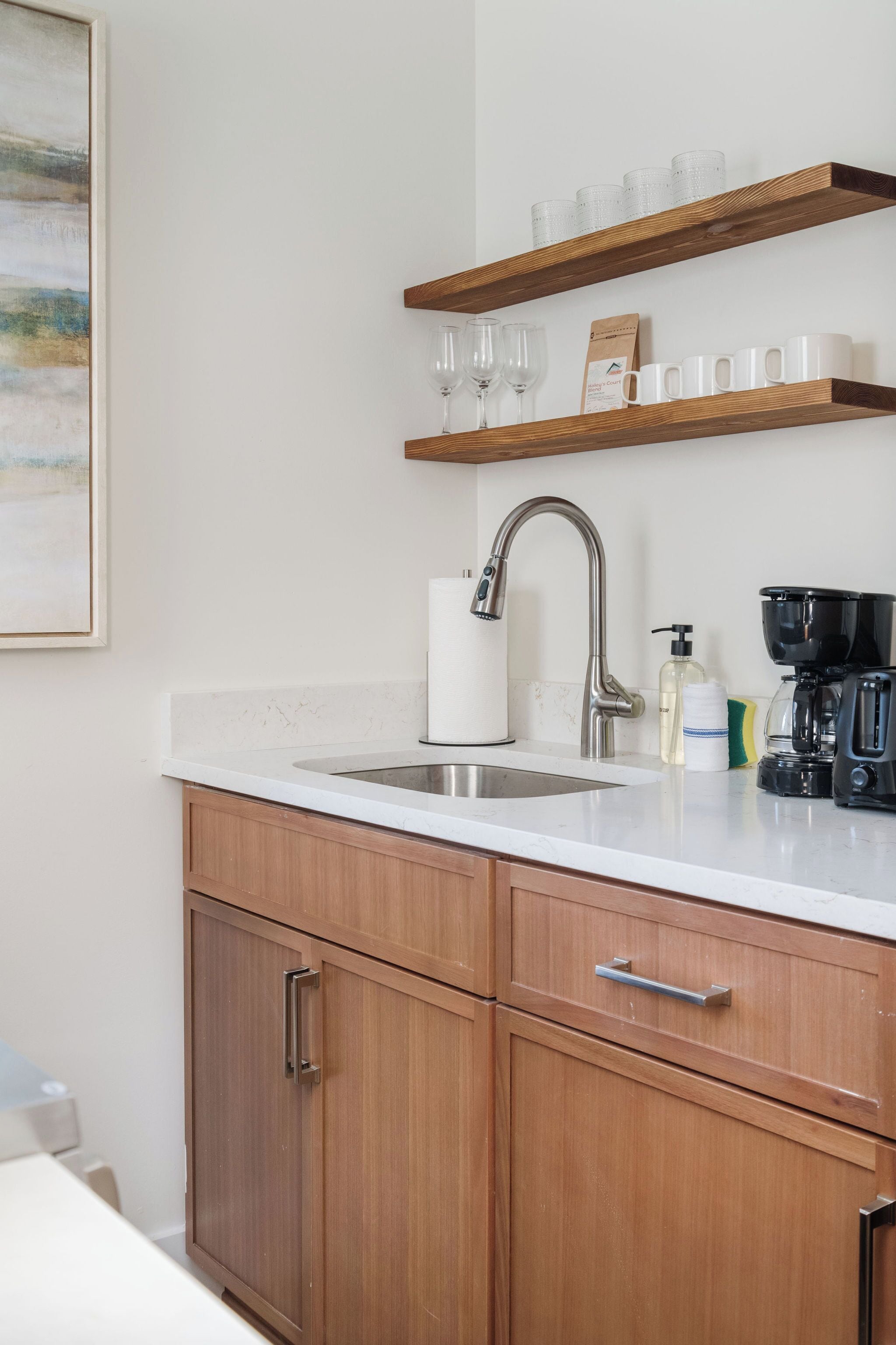 A kitchen with wooden cabinets, a white countertop, a stainless steel sink, and a coffee maker.
