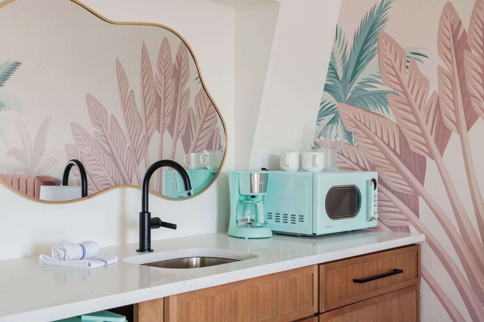 A modern bathroom with a sink, mirror, and a teal-colored coffee maker.