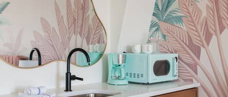 A modern bathroom with a sink, mirror, and a teal-colored coffee maker.
