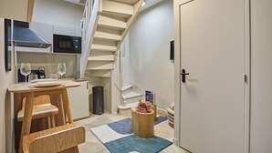 Une cuisine compacte équipée d’un micro-ondes, d’une petite table à manger et d’une chaise en bois. Un escalier mène à l’étage supérieur.