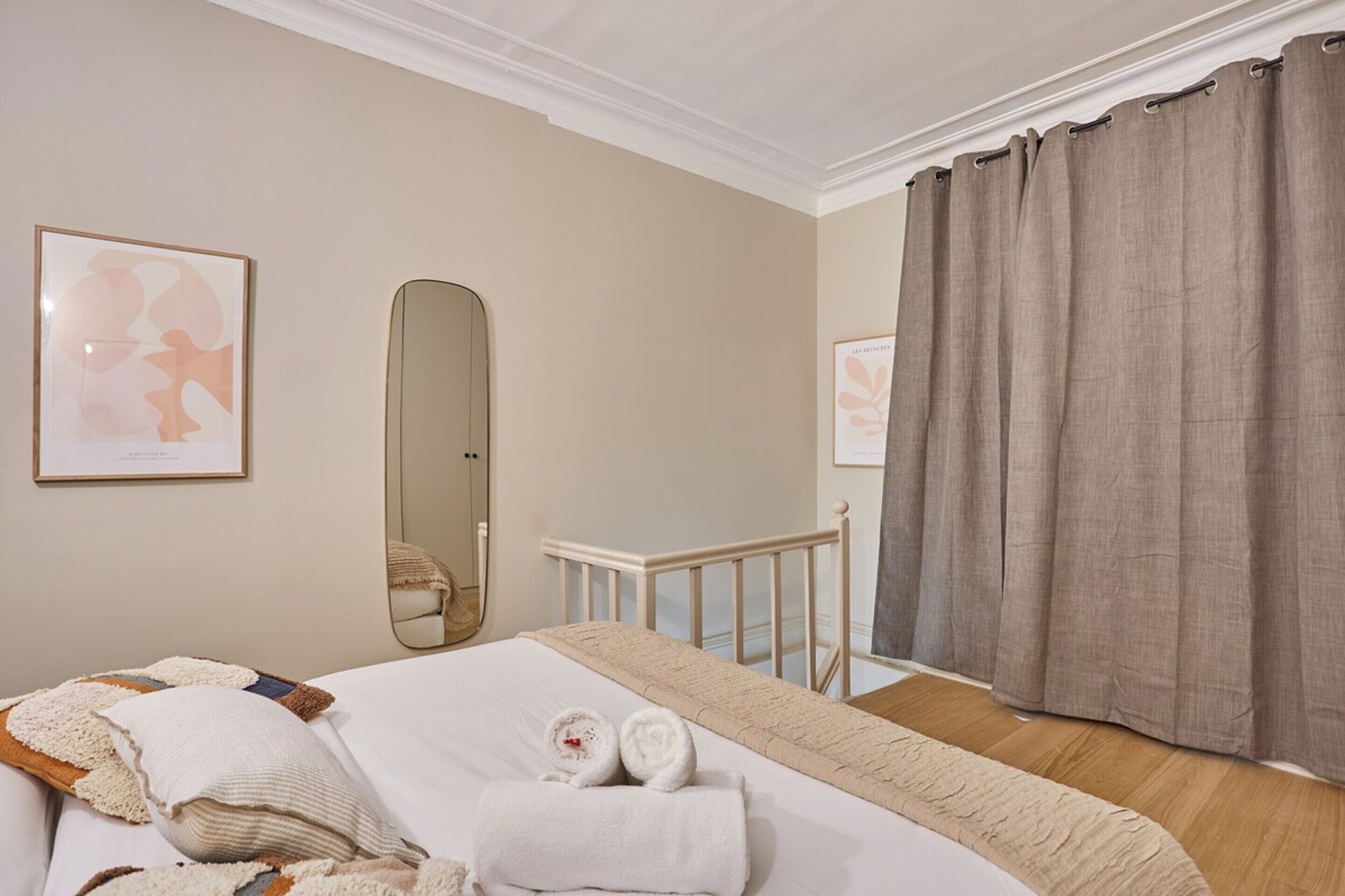 Une chambre d’hôtel avec un lit, une table de chevet, un miroir et une fenêtre avec des rideaux.