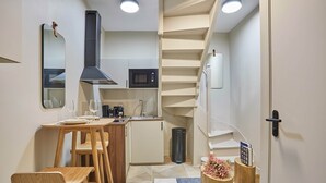 Une cuisine compacte équipée d’un four à micro-ondes, d’une cuisinière et d’un évier, une table à manger en bois avec des chaises, et un escalier menant à un autre niveau.