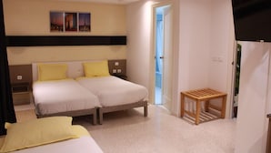 Habitación de hotel con dos camas, una mesita de madera, televisión y puerta que da a un balcón.