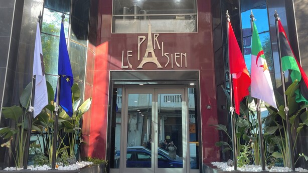 La entrada de un edificio con el letrero "Le Parisien" y varias banderas.