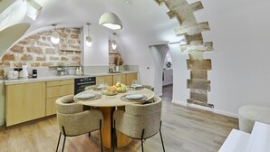 A modern kitchen with a stone wall backsplash, wooden cabinets, and a round dining table with wicker chairs. - Superb New Apartement Le Marais Place des Vosges (Paris)