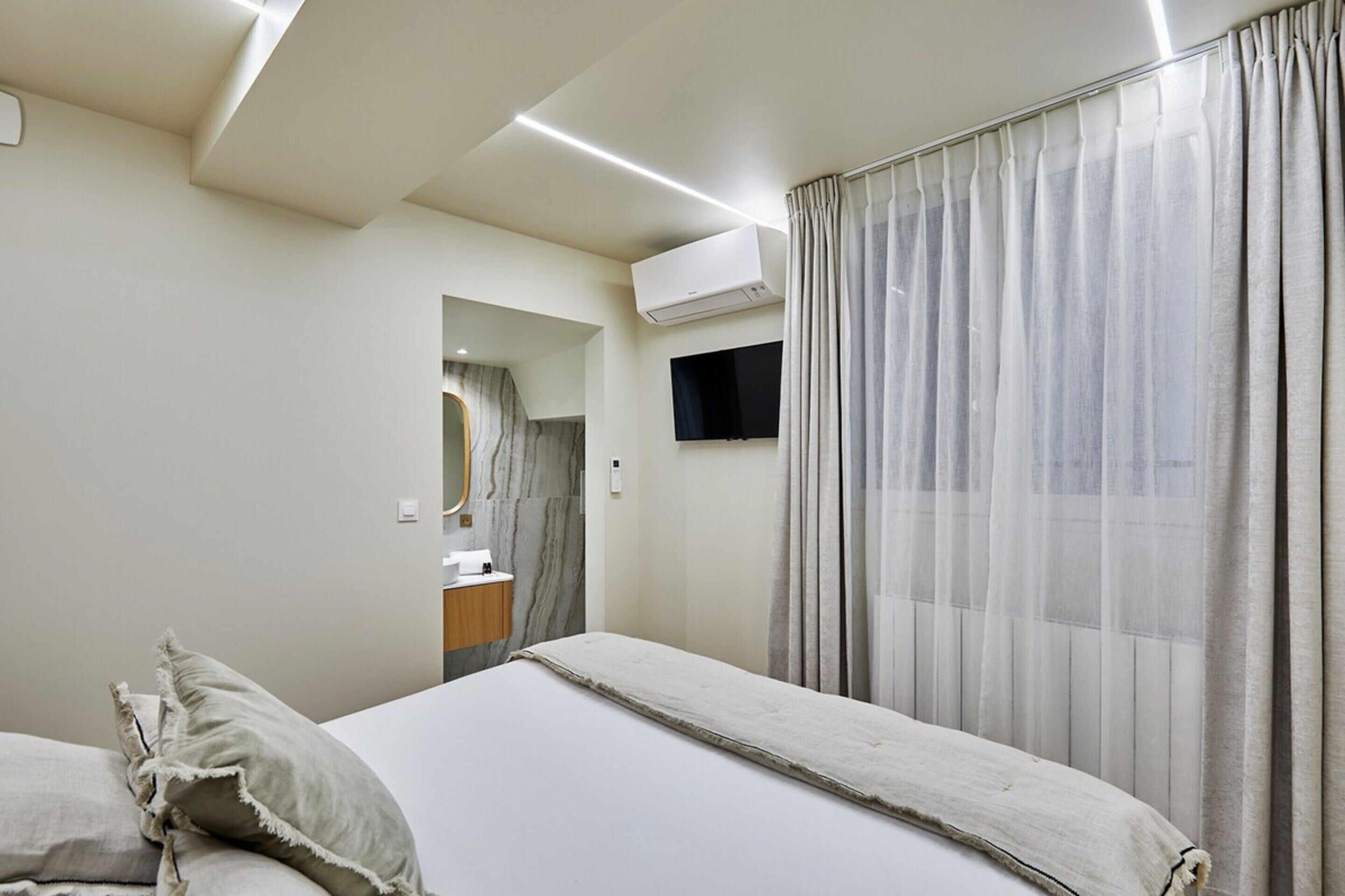 Una habitación de hotel moderna con una cama grande, un televisor de pantalla plana y un equipo de aire acondicionado.