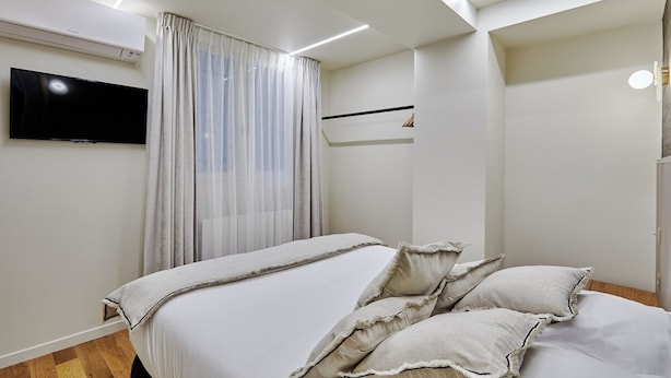 A modern bedroom with a bed, curtains, a mounted TV, and a ceiling light fixture. - Superb New Apartement Le Marais Place des Vosges (Paris)