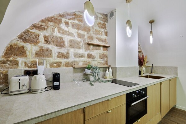 Une cuisine avec un mur en pierre, des meubles en bois, un plan de travail avec un évier et des appareils électroménagers modernes.