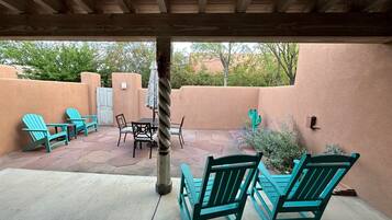 A covered patio with turquoise Adirondack chairs, a table, and a cactus.