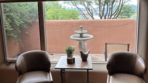 A room with a view of a fountain and trees, two leather chairs, a small table with a plant and a pitcher, and a window with blinds. - Casa Feliz is waiting for you!
 (El Prado)