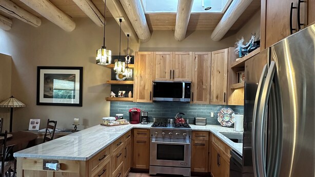 A kitchen with wooden cabinets, a stainless steel refrigerator, a microwave, and a stove. There is a skylight above the kitchen. - Casa Feliz is waiting for you!
 (El Prado)