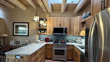 A kitchen with wooden cabinets, a stainless steel refrigerator, a microwave, and a stove. There is a skylight above the kitchen.