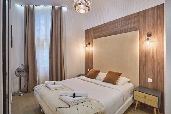 A modern bedroom with a large bed, bedside tables, a standing fan, and a wooden accent wall. - Superb Apartment Le Marais (Paris)