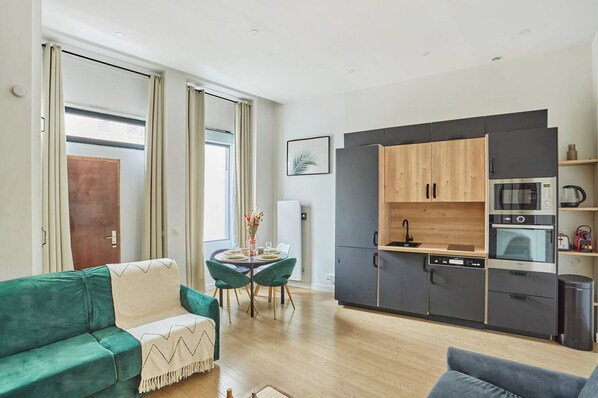 A compact living space with a kitchenette, a dining area with a table and chairs, and a green sofa. - Superb Apartment Le Marais (Paris)