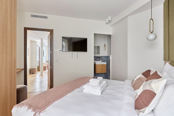 A modern hotel room with a neatly made bed, a flat-screen TV mounted on the wall, and a bathroom visible through an open door. - Exceptional Apartment With AC - Heart of Paris (Paris)