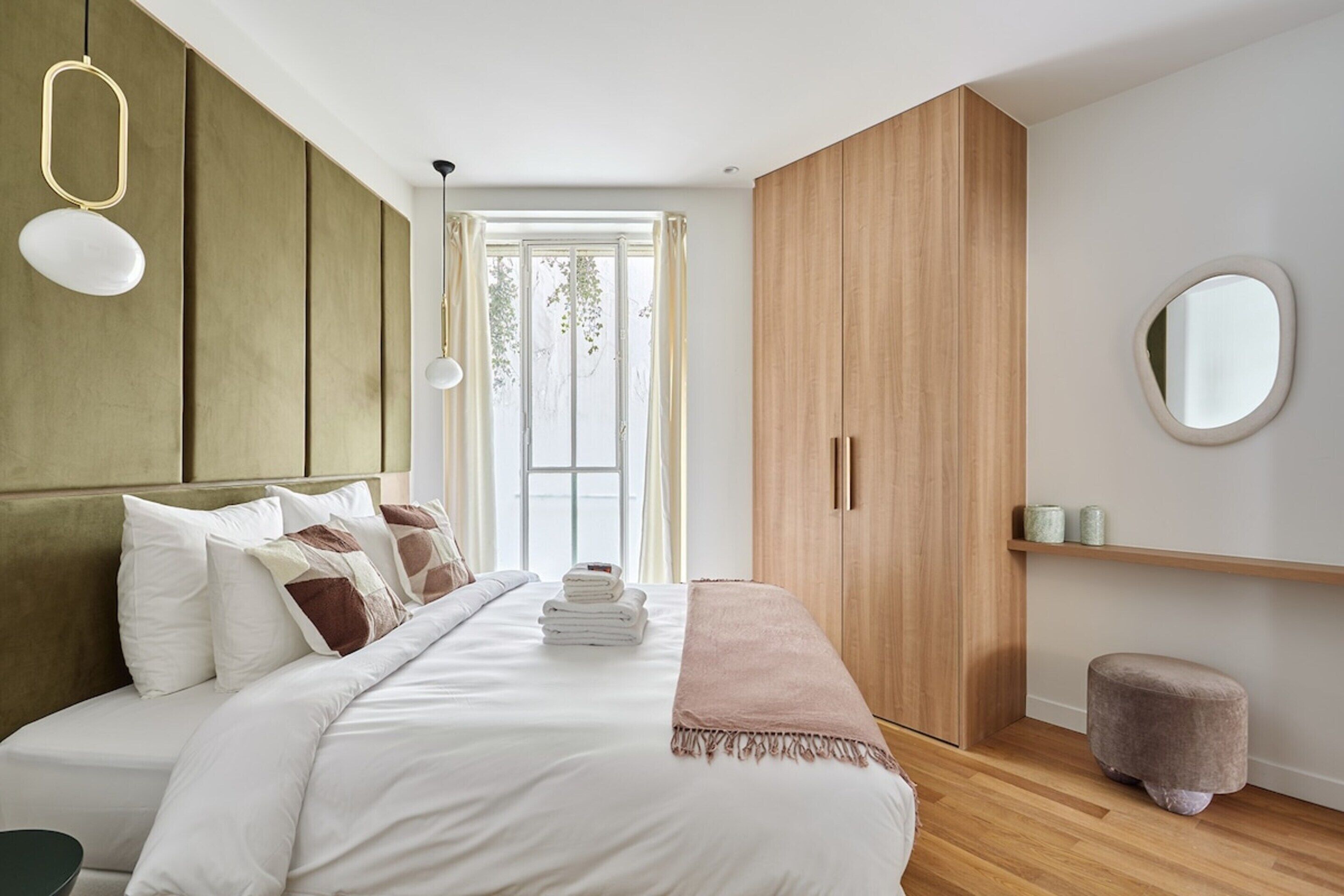 A modern bedroom with a large bed, wooden wardrobe, and a round mirror on the wall.